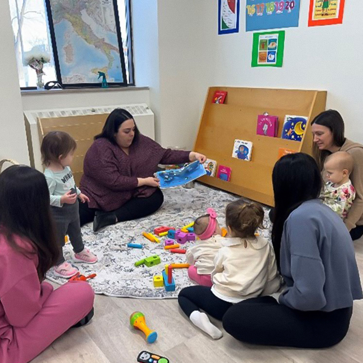 A Teacher and Mothers sitting with their kids in a classroom