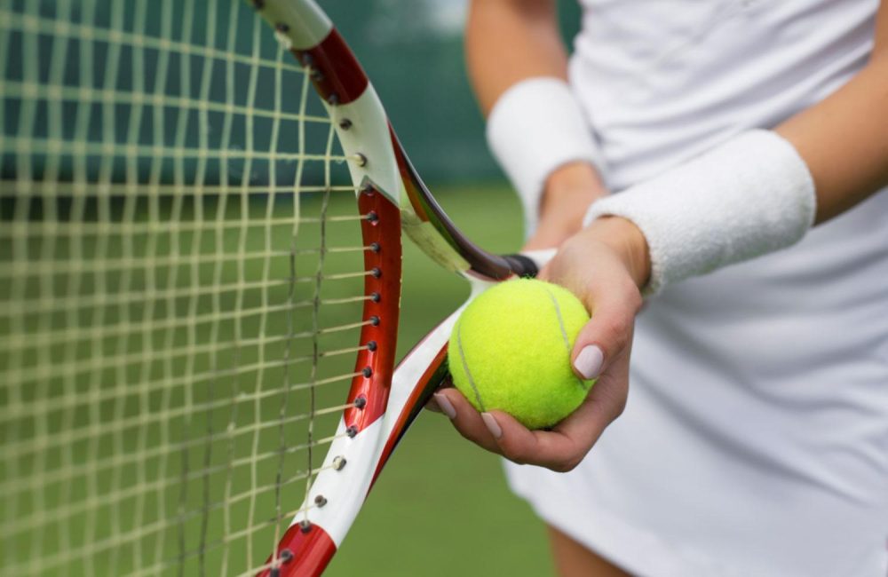 A female holds a tennis racquet and a tennis ball.