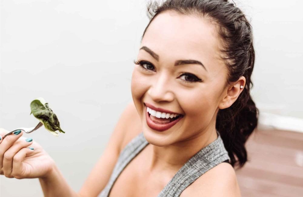 A female holds up a fork with spinach.